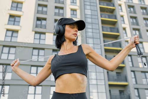 A woman in a black sports bra and cap holds a jump rope in front of an apartment building, ready for a workout
