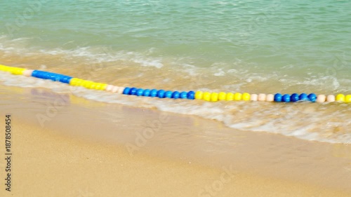 A line of colorful buoys on a sandy beach, bobbing on the coastal sea waves. The buoys create a safety zone for tourists.