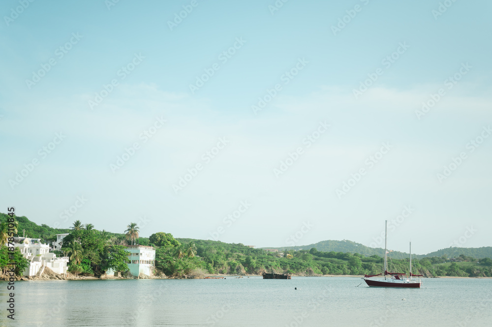 Fototapeta premium Sailboat anchored near lush shoreline and buildings in Vieques