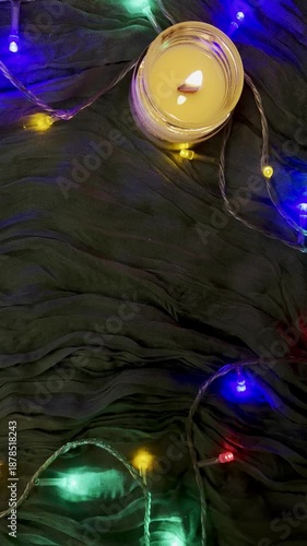 Magical background green fabric, colorful garlands and candle top view close-up