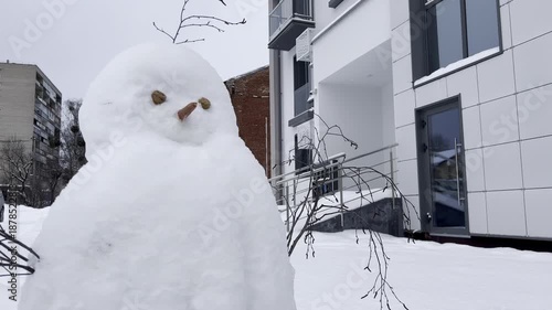 A cheerful snowman with a carrot nose, arms, and branches against the backdrop of a new building