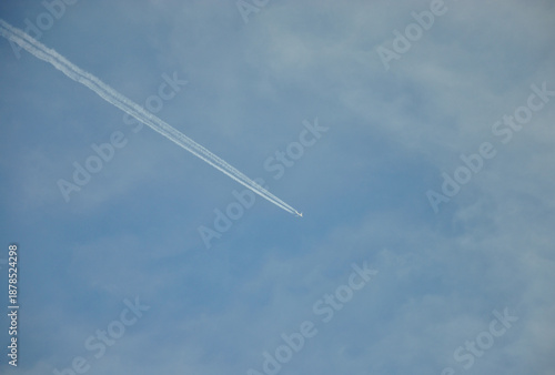 Passenger plane fly high in the sky leaving white smoke trail. Concept of travel, carbon footprint, and aviation industry. Minimalist shot of a single jet trail crossing a bright blue sky. 