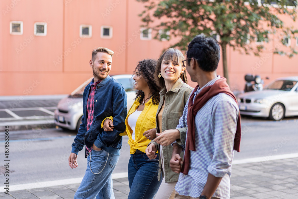 Fototapeta premium Group of young multicultural friends walking and laughing together in the city on a sunny day. Friendship, diversity and youth lifestyle concept.