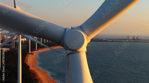 Coastal wind turbines spinning amidst sunset over industrial oil tanker harbor.