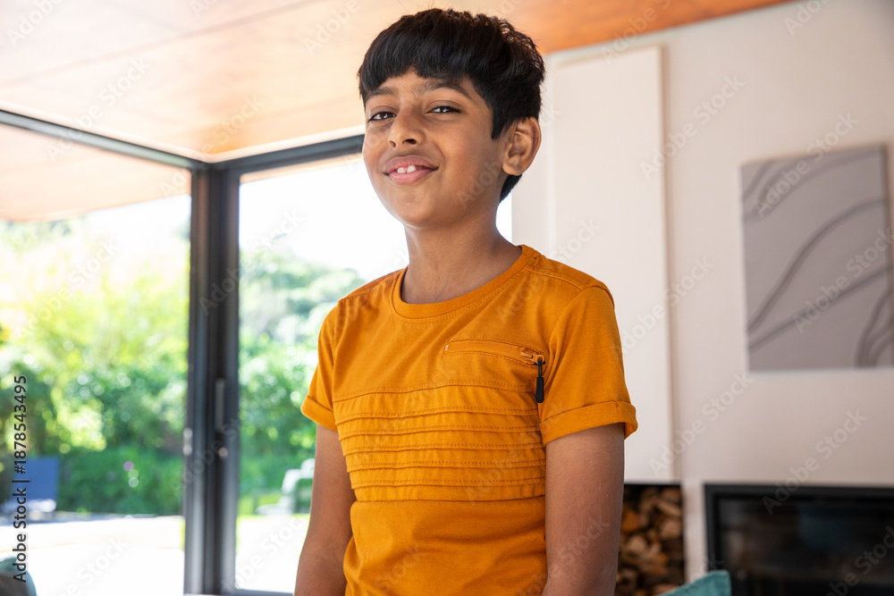 Naklejka premium Indian boy standing in living room in bright orange t-shirt with zip pocket under wood ceiling