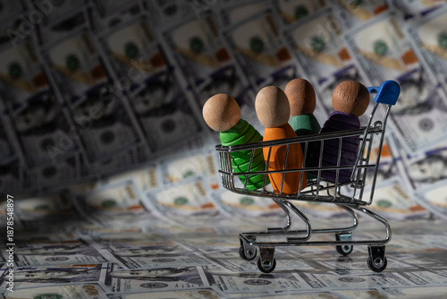 Symbolic wooden people in a miniature shopping cart against a backdrop of $100 bills