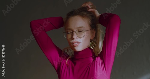 Close-up 4K footage of a sensual young beautiful Caucasian blonde woman with eyeglasses fixing her hair. Young blonde woman with glasses gently fixes her hair, exuding calm elegance and charm.