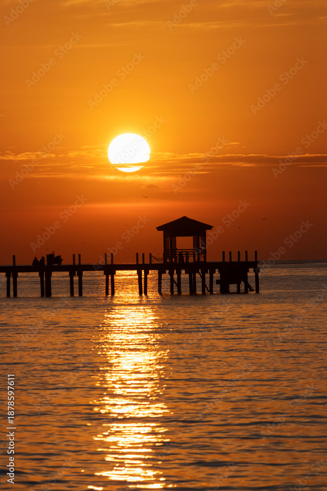 Fototapeta premium Golden sunset over calm sea with silhouetted wooden pier and gazebo reflecting warm light at Bang Pu in Samut Prakan, Thailand.