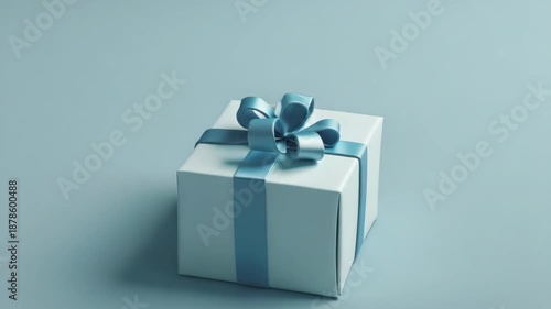 A white box with a blue ribbon on top. The ribbon is tied in a bow. The box is sitting on a table