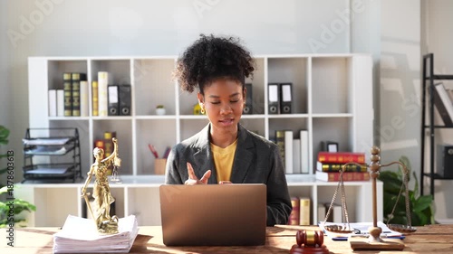 Professional female lawyer offering legal advice and consultation to a client via video conference call, sitting at her desk in a modern law office with a gavel and scales of justice