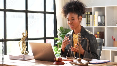 Professional african american female lawyer sitting at her desk in a modern law office, giving legal advice to a client during a video conference call on her laptop computer