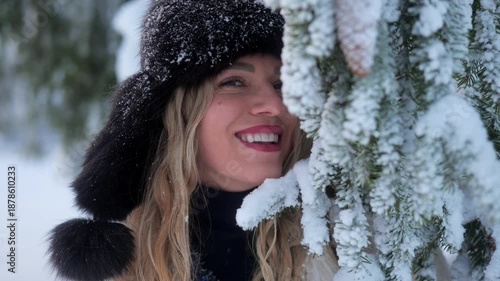 Woman smiling in snowy landscape with fur hat near evergreen trees during winter day