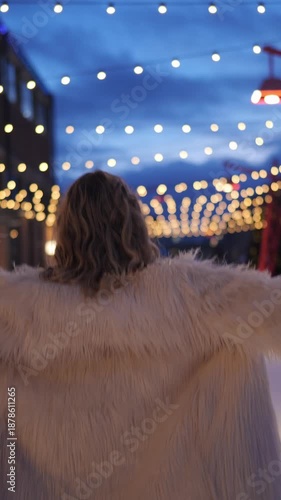 Woman running on snowy street with string lights during evening hours in a festive setting