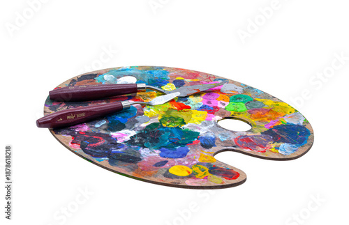 Isolated object for creativity. Oval wooden artist palette covered with colorful spots of dry and fresh paint, featuring two palette knives. Concept of art, hobby, painting, and inspiration