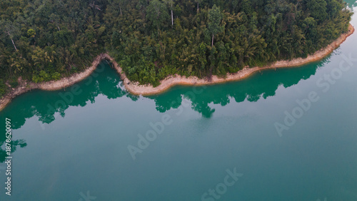 Aerial view of the lake's turquoise waters meeting the lush green forest of Khao Sok National Park, Surat Thani, Thailand.