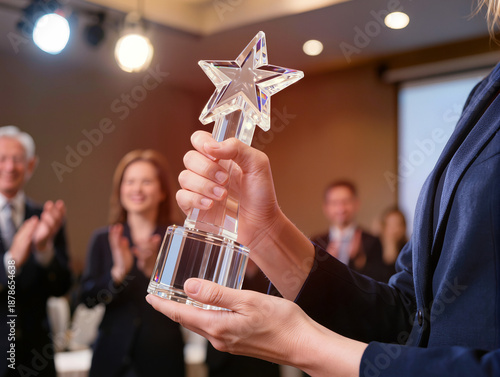 Close-up of a businesswoman holding a beautiful star-shaped crystal trophy with colleagues applauding in a blurred office meeting background, 