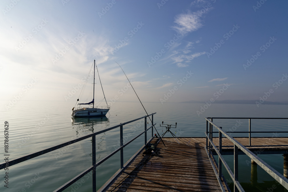 Obraz premium Sailboat moored at Balaton lake with fishing gear on the pier during early morning light