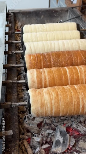Spinning cylindrical trdelnik dough slowly browning on grill, transforming into golden crispy pastry through traditional czech cooking method over warm coals vertical footage