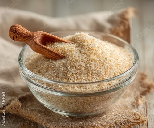 natural psyllium husk in a transparent glass bowl, small wooden scoop partially buried in the husks
