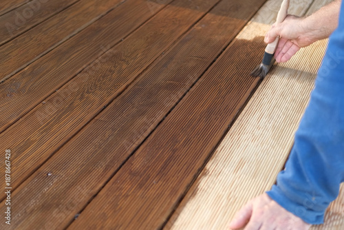 Brown oil for protection of wood by staining. Painting a larch for protecting and pests. Woodworker applying finish to terrace deck board. Repairman varnishing with brush wooden plank floor surface.