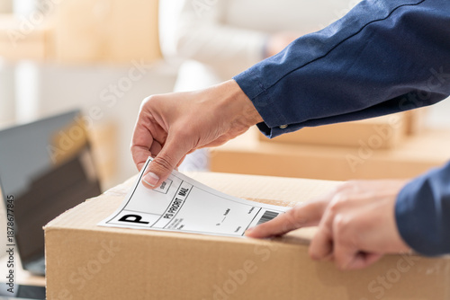 Business man preparing a package for shipping, sticking priority mail label on a cardboard box at his startup business office