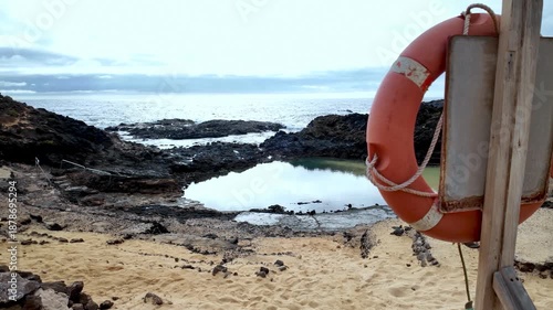 Lifebuoy hanging near a tidal swimming pool created by solidified volcanic lava on a sandy beach at the Charco del Palo nudist resort on the coast of Lanzarote, Canary Islands