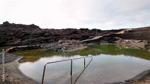 Stunning natural swimming pool formed by volcanic lava rock in the Charco del Palo nudist village, an iconic destination on the island of Lanzarote in the Canary Islands, Spain, during a cloudy day