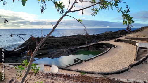 Scenic view of the natural volcanic pools and sandy beach at the nudist resort of Charco del Palo in Lanzarote, Canary Islands, Spain, with the Atlantic ocean in the background