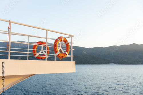 Bright orange lifebuoys on white passenger ship railing with calm blue sea and green coastal hills in background, soft evening light during peaceful Greek ferry crossing between mainland and islands
