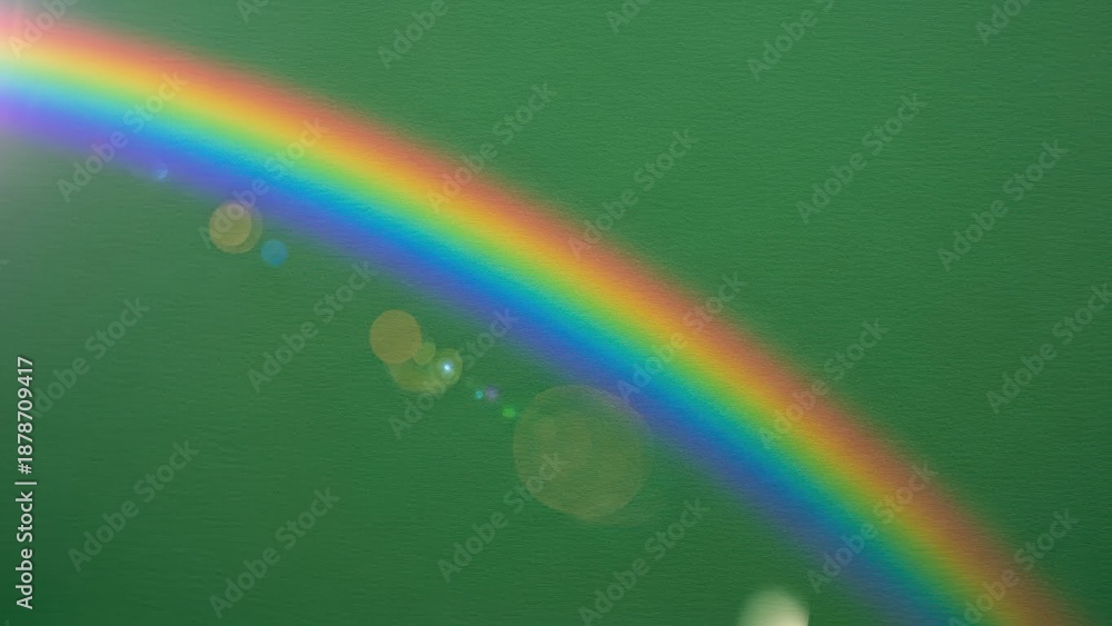 Fototapeta premium Rainbow arc across green background for Saint Patrick day. Vibrant color spectrum light flare on textured surface for Irish celebration.
