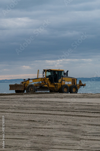 Heavy bulldozer leveling sand on coastal beach, construction and maintenance work near the sea.