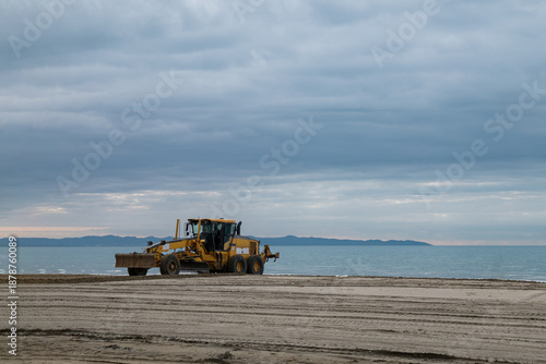 Construction bulldozer operating on sandy coastline, beach maintenance and infrastructure work near the sea.