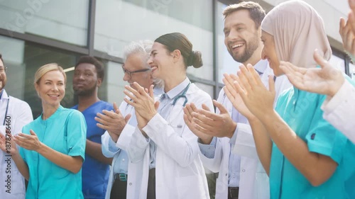 Smiling medical staff clapping hands while standing outside clinic under bright daylight. Confident group celebrating progress and sharing uplifting energy. Professionals enjoying supportive moment.