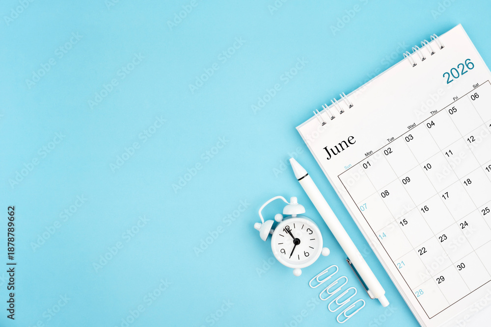 Fototapeta premium June 2026, Monthly desk calendar for 2026 year and alarm clock with paper clips on blue color background.