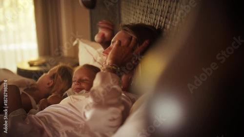 A serene morning as a mother and her two young children gently wake up in a luxurious bed during their peaceful family vacation at an opulent island resort.