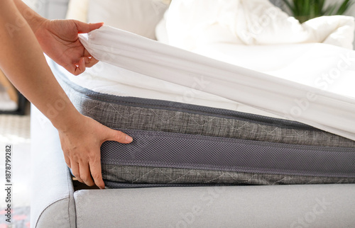 Changing bed sheets. Woman is putting on a fitted white cotton sheet on a mattress while making the bed. 