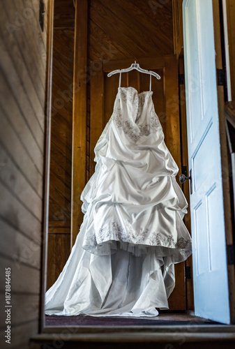 Long White Wedding Dress Hanging in Wooden Doorway