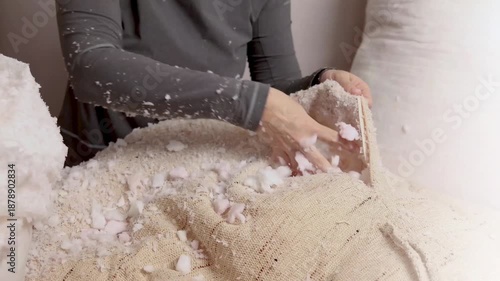 Woman fills a pillow case with foam rubber. Foam pieces, crumbs. Woman repairs furniture pillows. White polyurethane foam rubber pieces. stuffing for pillows and furniture. Cropped footage