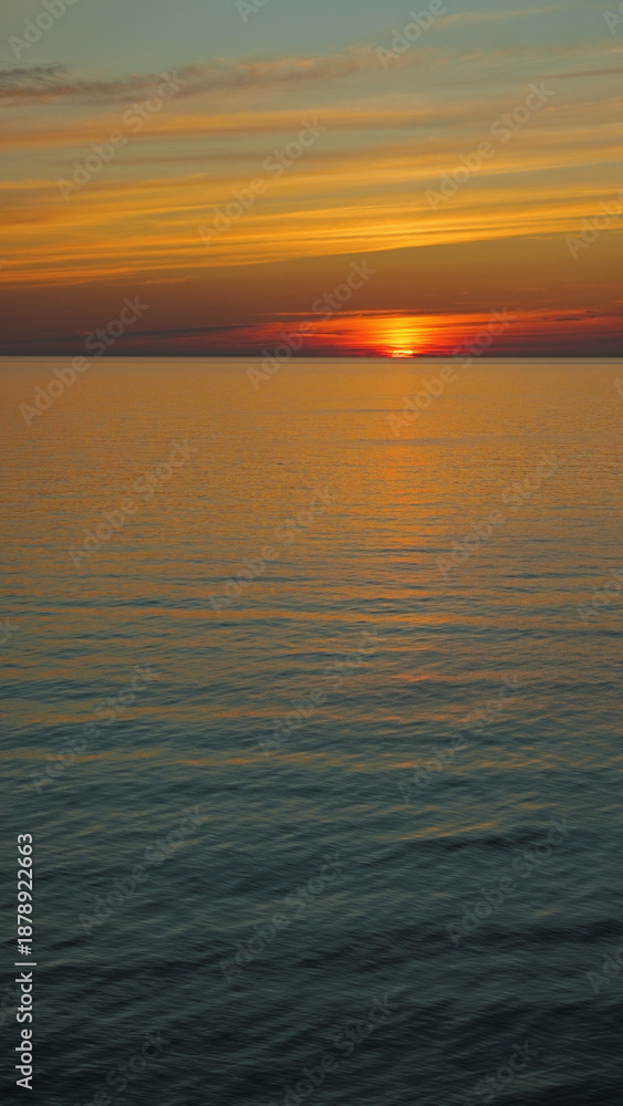 Obraz premium Golden sunset over a calm ocean with vibrant streaked clouds