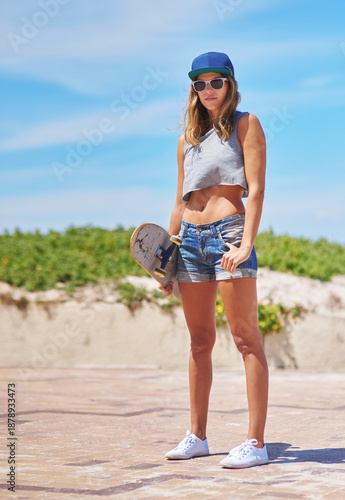 Confident, woman and skater with skateboard on beach outdoor for fashion statement, sunglasses and travel adventure. Pride, female person and streetwear clothes, trendy activity and summer transport