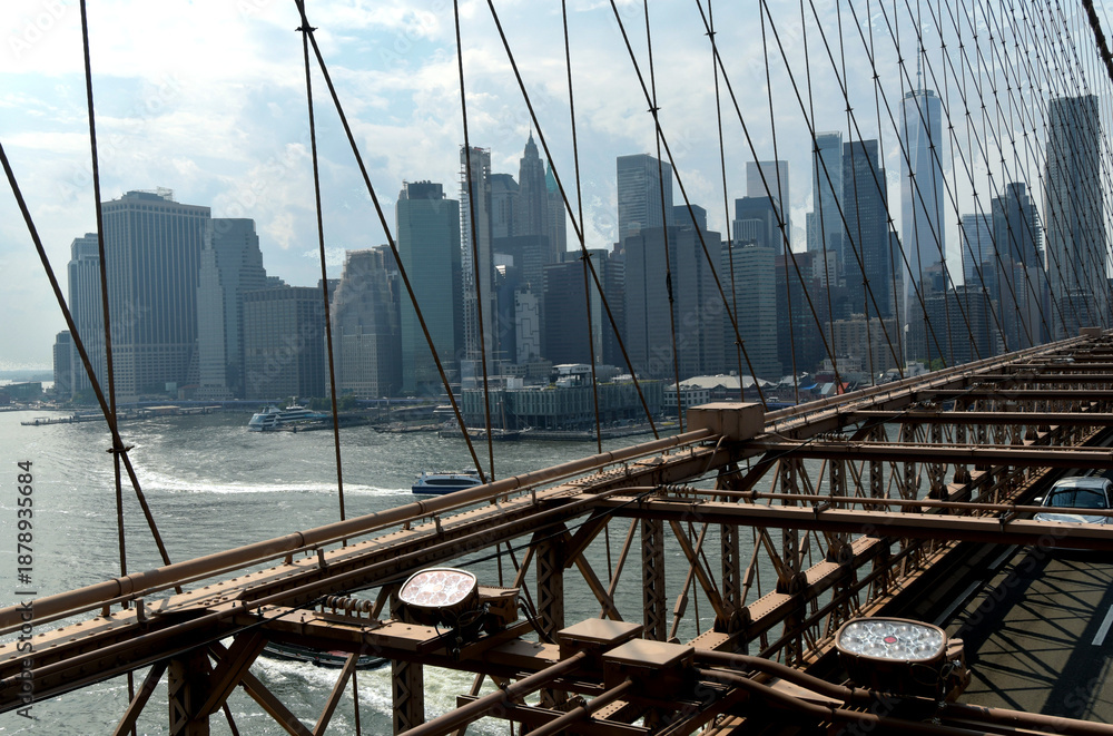 Naklejka premium The Brooklyn Bridge, built in 1883, is the first suspension bridge constructed of steel and overlooks the skyscrapers of Manhattan, the Big Apple.