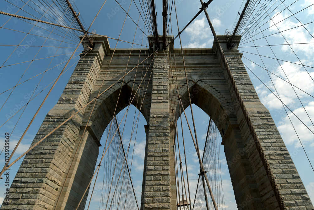 Fototapeta premium The Brooklyn Bridge, built in 1883, is the first suspension bridge constructed of steel and overlooks the skyscrapers of Manhattan, the Big Apple.
