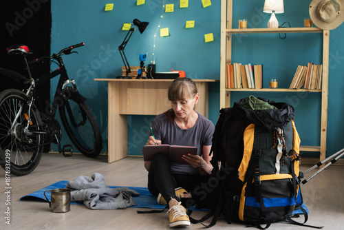 Female tourist backpacker making checklist while preparing to hiking tour at home