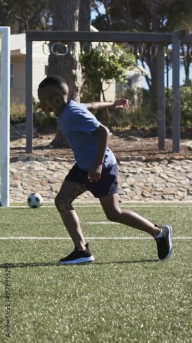 Vertical video: Boy in blue shirt practicing right-foot shots with ball at feet on turf toward goal