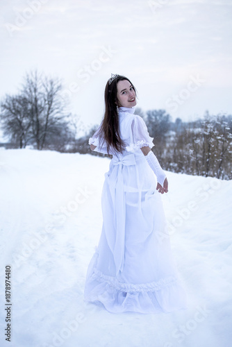 Snow Queen. A young girl in a white dress in the snow. Girl in a white dress. Bride. Winter cold weather. Model. Young woman in winter park.