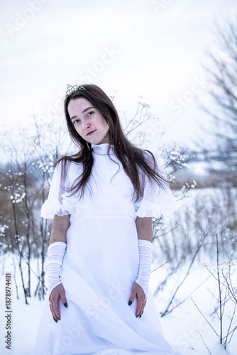 Snow Queen. A young girl in a white dress in the snow. Girl in a white dress. Bride. Winter cold weather. Model. Young woman in winter park.