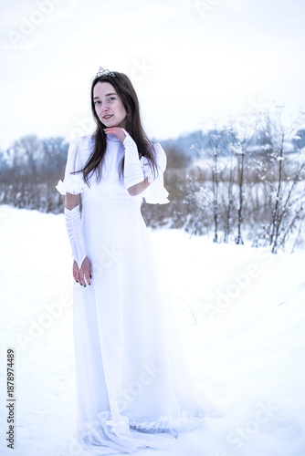 Snow Queen. A young girl in a white dress in the snow. Girl in a white dress. Bride. Winter cold weather. Model. Young woman in winter park.