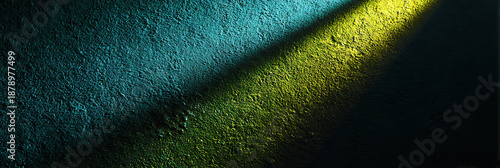 A textured wall illuminated by a narrow beam of contrasting light, revealing rich hues of blue and green, creating a dramatic interplay of color and shadow.
