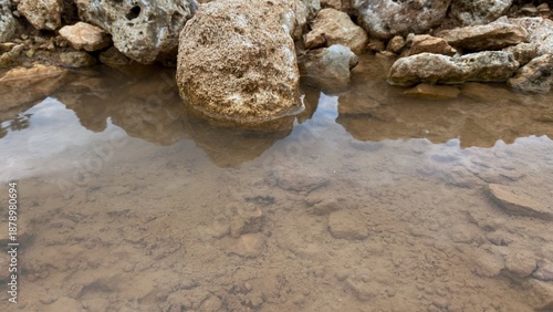 Canvas-taulu A pool of clear water with natural rocks reflecting the water's surface, showcasing the texture of the soil and the calming feel of nature