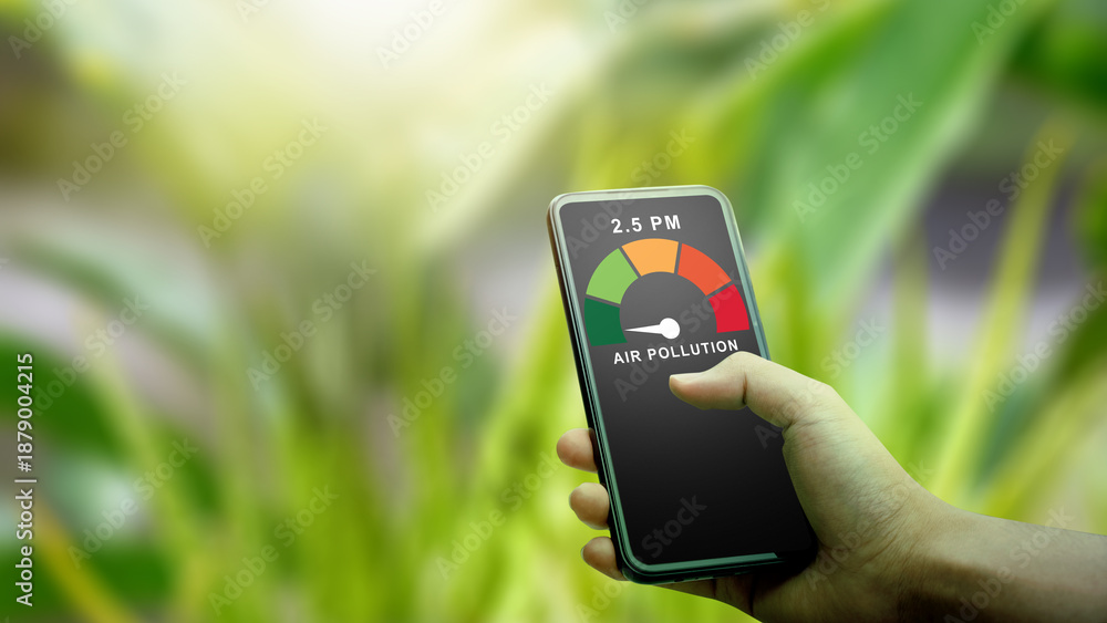 Fototapeta premium A person checks high air pollution levels and PM2.5 on a mobile app while outdoors. The digital gauge shows poor air quality against a blurred green plant background